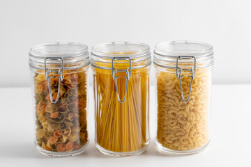 food storage, eating and cooking concept - close up of jars with different pasta types on white background