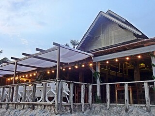 Seaside restaurant with outdoor seating area by the shore during dusk.