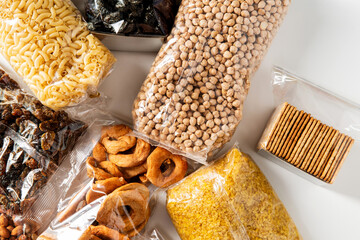 food storage and healthy eating concept - close up of bags with dried fruits, cereals, pasta and nuts on white background, top view