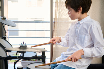 Authentic portrait of Hispanic teenager boy using drumsticks, beating on the drum while performing...