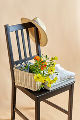 home decor and design concept - flowers in basket, clothes, hat and magazines on vintage chair over beige background