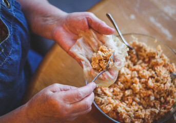 The hands of a senior woman hold a raw leaf of sauerkraut and put a metal teaspoon of rice-meat