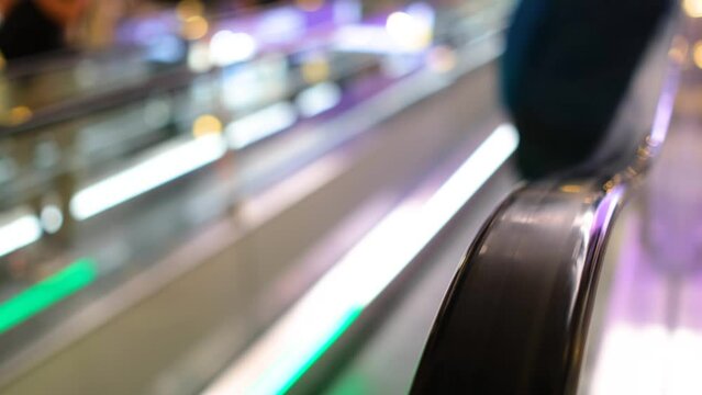 detail of the handrail of an escalator in a shopping mall. In the background pass out of focus people anonymously shopping.