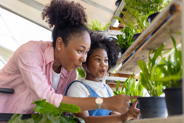 African mother and daughter is choosing tropical fern and ornamental plants from the local garden center nursery during summer for weekend gardening and outdoor - obrazy, fototapety, plakaty