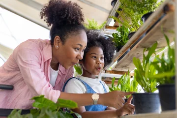Deurstickers African mother and daughter is choosing tropical fern and ornamental plants from the local garden center nursery during summer for weekend gardening and outdoor © Akarawut