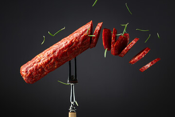 Traditional smoked salami sausage on a fork sprinkled with rosemary.
