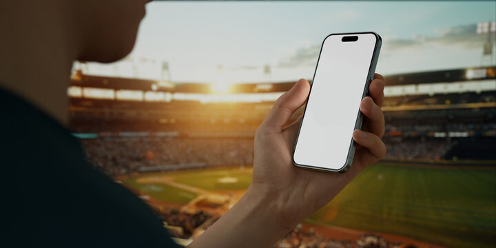 A hand holds a smartphone with a green screen at a baseball stadium