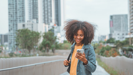 Happy young African American woman using social media on mobile phone on street in a urban city....