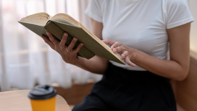 Cropped image of woman enjoying reading a good book Holding an open book and a cup of coffee on the table.