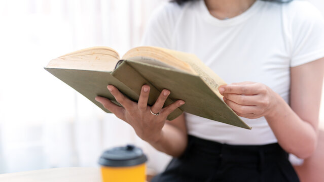 Cropped image of woman enjoying reading a good book Holding an open book and a cup of coffee on the table.