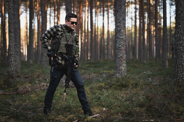 Male private soldier with a modern assault rifle and body armor in the forest.