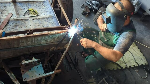 Welding work: a man welds metal using a welding machine while wearing a protective mask. Repairing metal equipment.