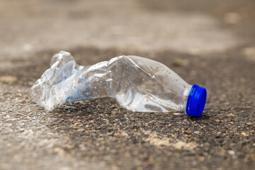 plastic bottle is laying on the ground, broken and discarded