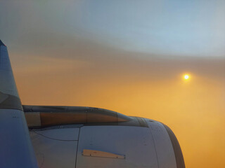 Beautiful orange sunrise from airplane window with engine and plane wings in view.
