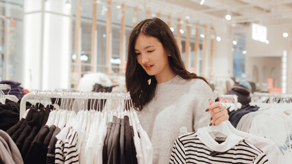 Korean teenage girl choosing and buying trendy clothes in a shopping mall. Retail and consumerism. Sale promotion and shopping concept. Part of a series - 772393582