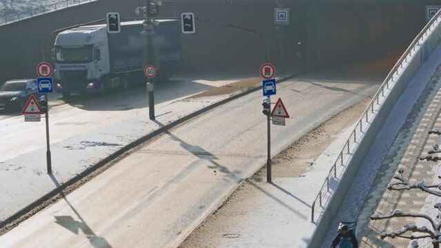 Cyclist on snowy road with traffic signs and truck near underpass in sunlight
