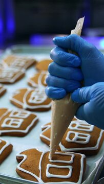 Gingerbread houses being decorated with icing. White glazing being squeezed from a pastry bag on the beautiful cookies. Close up. Vertical video
