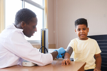 african american man pediatrician doctor measuring blood pressure  and exam a boy from sickness in the office at the hospital. medical and healthcare services.