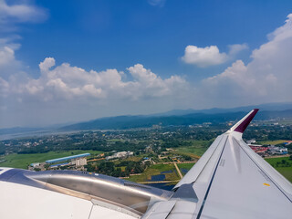 Beautiful view of the cityscape with mountain, forest, Cloudscape, and water bodies captured from an airplane window while taking off along with a view of aircraft wing and engine.