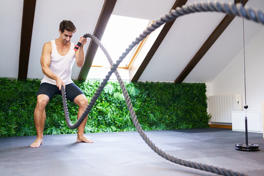 Strong sportsman exercising with battle ropes