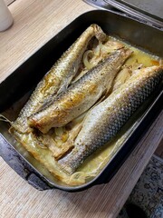 Baked mullet fish with onions in its own sauce lies on a baking sheet on the table after cooking. Close-up.