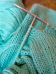 Female hobby knitting. Yarn in turquoise color And knitting needles. The beginning of the process of knitting a women's sweater.