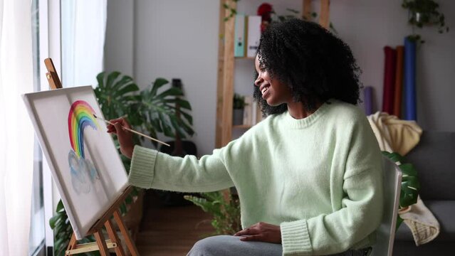 Young African American woman painting a picture in her living room feels a sense of accomplishment and pride - mental health inspiration