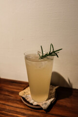cold iced lemonade on a glass being placed by the wall on a wooden table with a vase at the back