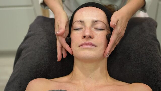 Professional beautician massaging face of woman with crystals