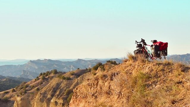 Red touring bicycle loaded with heavy gear in four pannier bags stand on hilltop viewpoint surrounded by deserted nature outdoors. Solo adventure bicycle touring travels