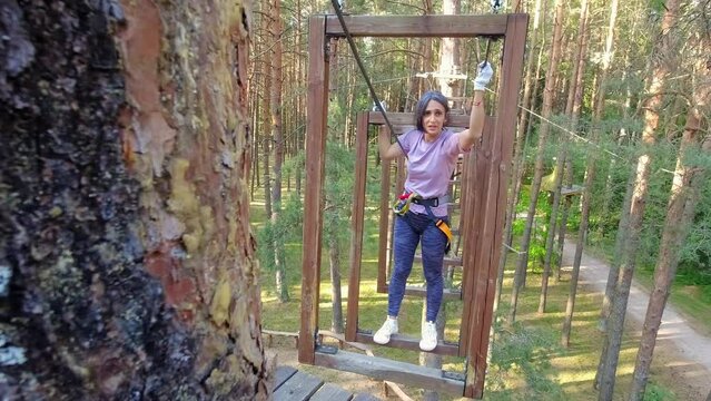 HBH,Palanga, Lithuania -2023:woman solo in adventure park challenging obstacle tracks. Struggle passing physical climbing section. Fear of heights.Challenge track in adventure park