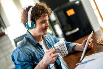 Latino man wearing headphones and talking to someone while drinking a hot beverage