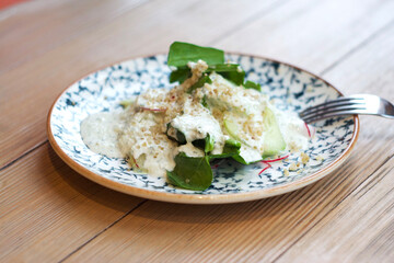 Salad of leaves, cucumber, radish and sauce in a plate on the table