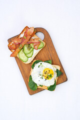  Sandwiches with fried eggs, fried ham, tomatoes, cucumbers, pepper on cutting board on white background, top view.