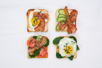  Sandwiches with fried eggs, fried ham, tomatoes, cucumbers, pepper on white background, top view.