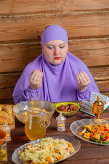 A Muslim woman in a purple hijab at the table for the holiday of Eid al-Fitr says bismi llah...