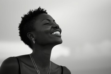 Black and white portrait of a joyful woman with short hair smiling against a cloudy sky background.