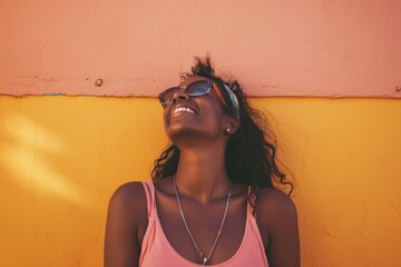 Joyful woman smiling in sunglasses against a vibrant yellow wall, depicting happiness and summer vibes.