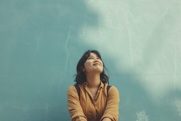 Smiling woman looking up, against a blue textured wall, expressing hope and positivity.