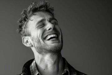 Black and white portrait of a joyful young man laughing with closed eyes, expressing genuine happiness.