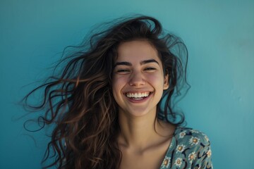Joyful young woman with flowing hair laughing against a blue background, expressing happiness and positivity.