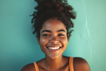 Portrait of a joyful young woman with a bright smile against a turquoise background.