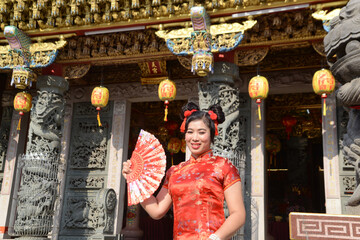 Portrait pretty Asian female in red traditional Chinese costume holding a fan standing and posing in the shrine.