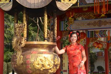 Portrait of a beautiful Asian woman in a red Chinese dresses pose and standing in front of a large incense burner inside a shrine.