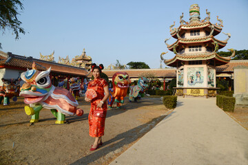 Portrait of a beautiful Asian woman in a red Chinese dresses pose and standing in front of Cinese pagoda inside a shrine.