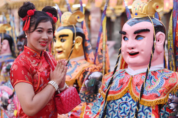 Portrait of pretty Asian woman in a red Chinese dresses worship in front of the warlord god puppet inside a shrine.