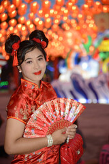 Portrait pretty Asian female in red traditional Chinese costume holding a fan standing and posing in front of the lanterns in the shrine.