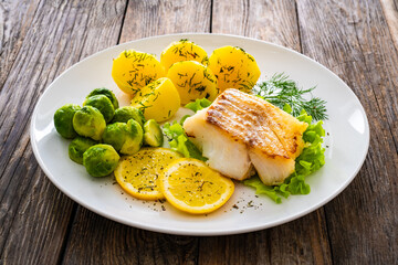 Fried cod loin, boiled potatoes and cooked Brussels sprouts on wooden table
