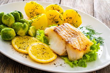 Fried cod loin, boiled potatoes and cooked Brussels sprouts on wooden table
