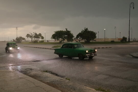 Old green almendron cars -yank tank, Ford classics from 1949 and 1953- drive down Marina Street in the hard rain of a tropical storm. Havana-Cuba-122